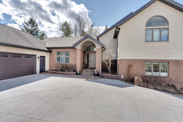 view of front of home featuring a garage, brick siding, driveway, and roof with shingles