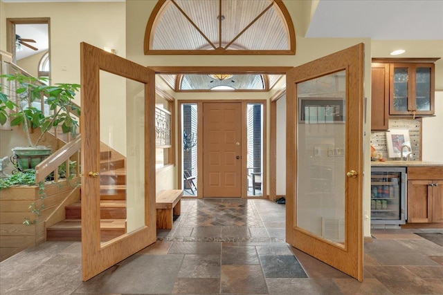 foyer entrance featuring visible vents, beverage cooler, stairway, a towering ceiling, and stone tile flooring