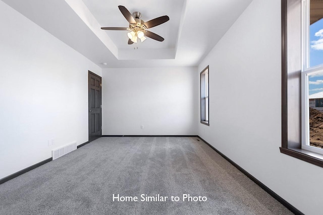 empty room with visible vents, baseboards, carpet, a raised ceiling, and ceiling fan