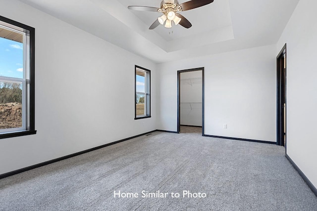 spare room with a raised ceiling, light colored carpet, baseboards, and ceiling fan