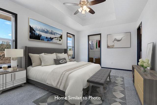 bedroom with carpet, baseboards, ceiling fan, a walk in closet, and a raised ceiling