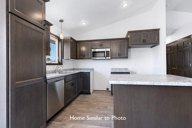 kitchen with dark brown cabinets, decorative light fixtures, vaulted ceiling, stainless steel appliances, and a sink