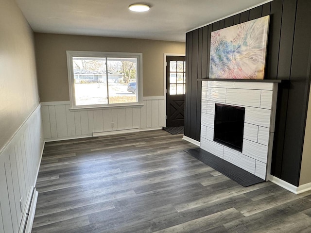 unfurnished living room with a baseboard radiator, a wainscoted wall, wood finished floors, and a fireplace