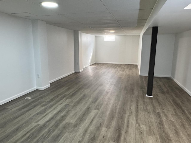 below grade area with baseboards, a paneled ceiling, and dark wood-style floors