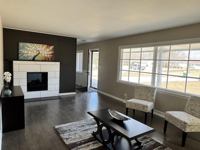 living area with a tiled fireplace, dark wood-style floors, and baseboards