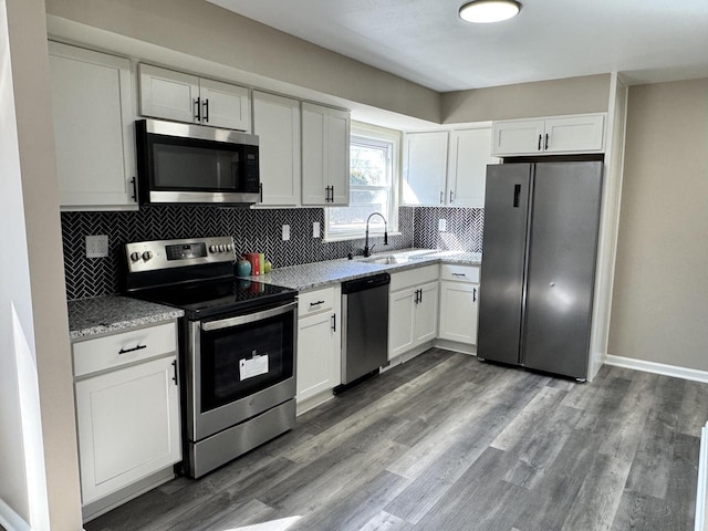 kitchen with dark wood finished floors, a sink, appliances with stainless steel finishes, white cabinetry, and backsplash