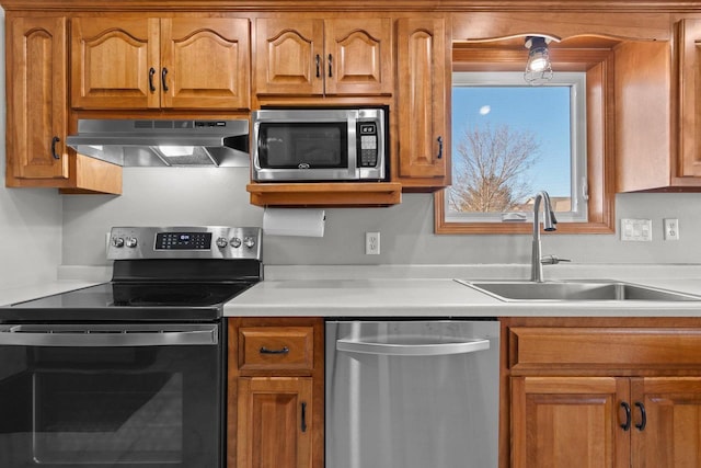 kitchen with under cabinet range hood, light countertops, appliances with stainless steel finishes, brown cabinetry, and a sink