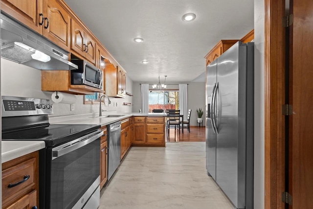 kitchen featuring brown cabinetry, a peninsula, a sink, stainless steel appliances, and under cabinet range hood