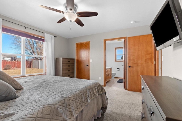 bedroom with ceiling fan, light colored carpet, and connected bathroom