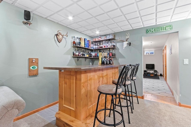 bar featuring light tile patterned flooring, a dry bar, a paneled ceiling, and baseboards