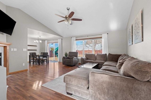 living area featuring baseboards, vaulted ceiling, ceiling fan with notable chandelier, wood finished floors, and a glass covered fireplace