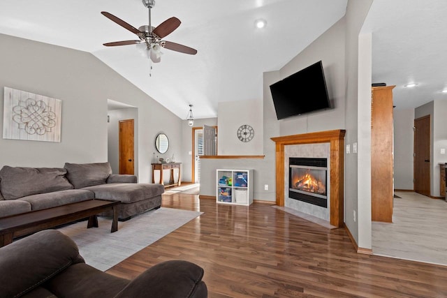 living room with a ceiling fan, vaulted ceiling, wood finished floors, and a tile fireplace