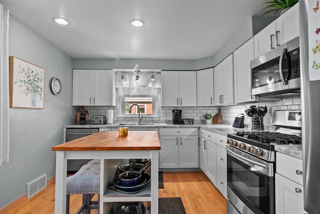 kitchen with visible vents, a sink, stainless steel appliances, butcher block counters, and decorative backsplash