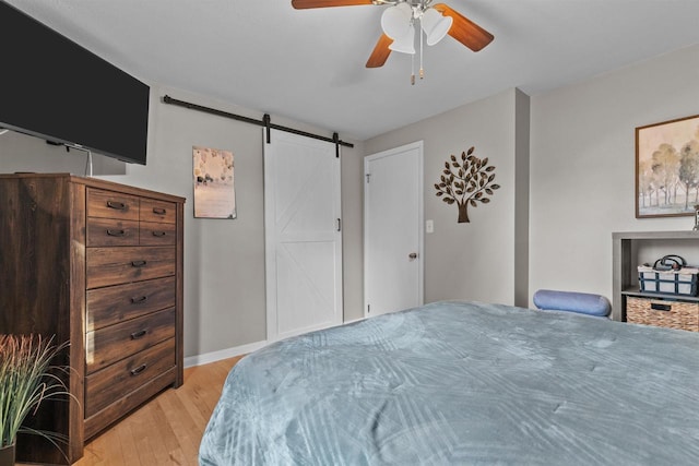 bedroom featuring light wood finished floors, baseboards, a barn door, and a ceiling fan