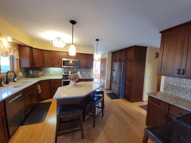 kitchen with light wood-type flooring, a sink, light stone counters, backsplash, and stainless steel appliances