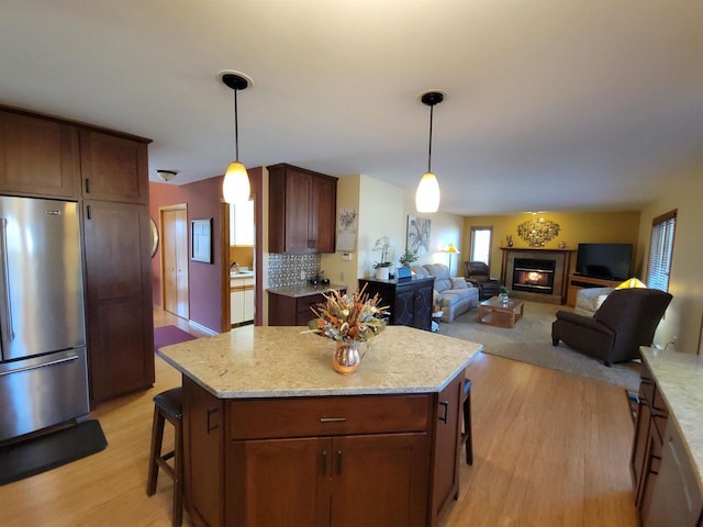 kitchen featuring light wood finished floors, a glass covered fireplace, hanging light fixtures, and freestanding refrigerator