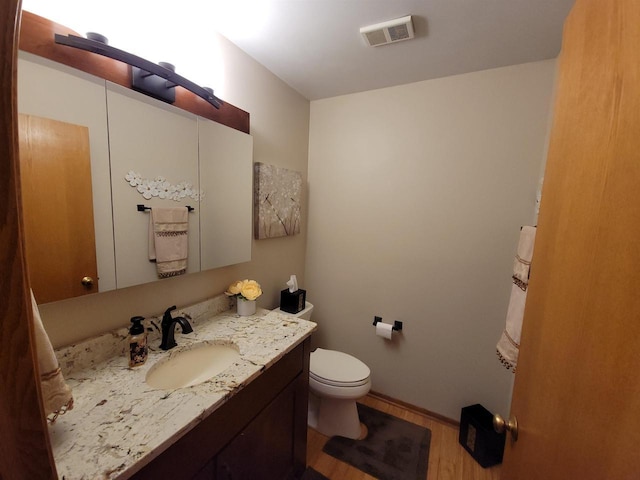 bathroom featuring visible vents, baseboards, toilet, wood finished floors, and vanity