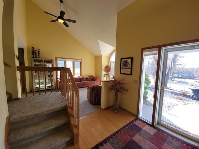 stairway with a ceiling fan, wood finished floors, and high vaulted ceiling