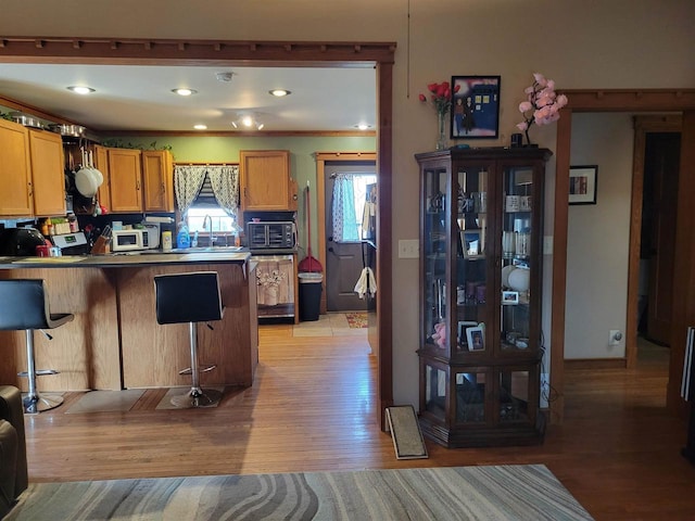 kitchen with white microwave, a peninsula, a breakfast bar area, and light wood-type flooring