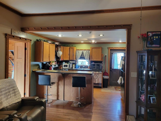 kitchen featuring white microwave, light wood finished floors, a peninsula, and a sink