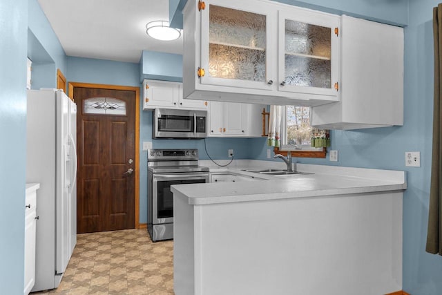 kitchen featuring light floors, a peninsula, a sink, light countertops, and appliances with stainless steel finishes