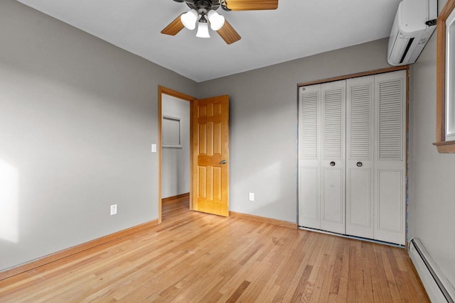 unfurnished bedroom featuring a wall mounted AC, a baseboard heating unit, a closet, wood-type flooring, and baseboards