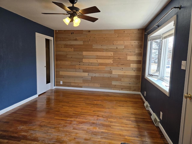 unfurnished room with visible vents, baseboards, wood finished floors, and wood walls