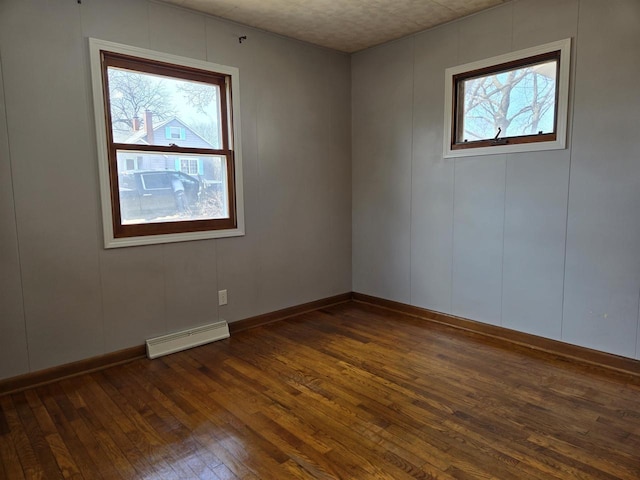 empty room with a wealth of natural light, a baseboard radiator, baseboards, and dark wood finished floors