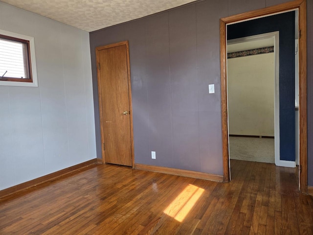 empty room with baseboards, wood-type flooring, a textured ceiling, and a decorative wall