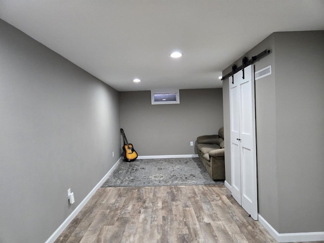 interior space with visible vents, baseboards, a barn door, recessed lighting, and wood finished floors