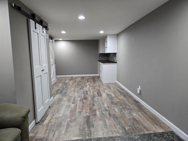 below grade area featuring recessed lighting, a barn door, baseboards, and light wood finished floors