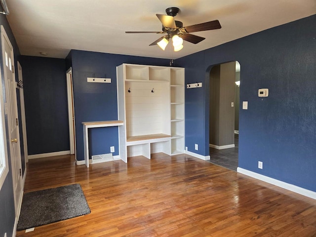 unfurnished living room featuring baseboards, arched walkways, wood finished floors, and a ceiling fan