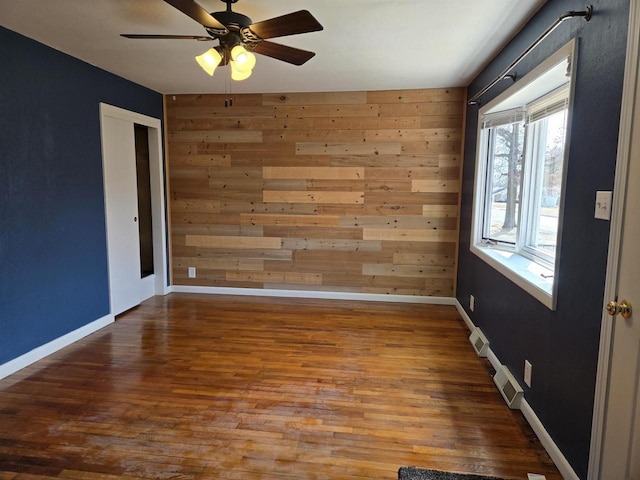 empty room featuring wood finished floors, baseboards, and wood walls