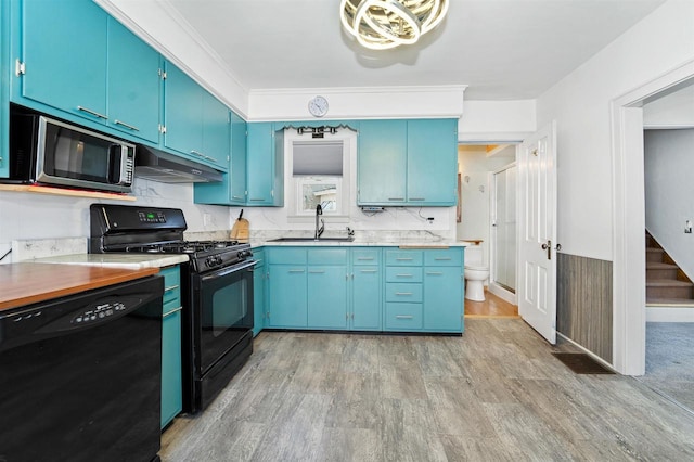 kitchen featuring blue cabinetry, light wood-style flooring, a sink, black appliances, and under cabinet range hood