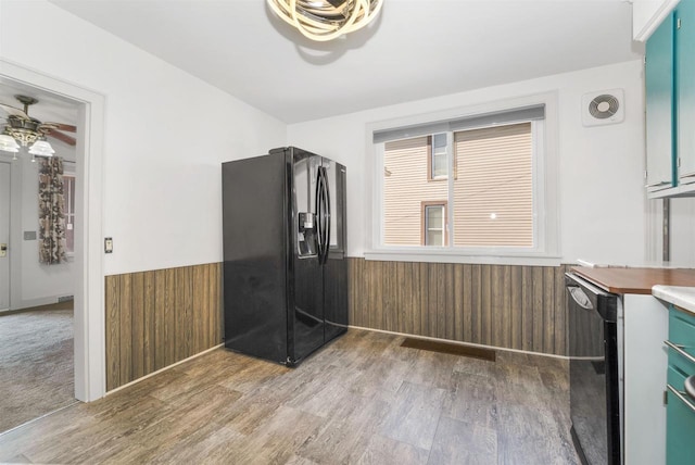 kitchen featuring a wainscoted wall, black fridge with ice dispenser, dishwasher, and wood walls