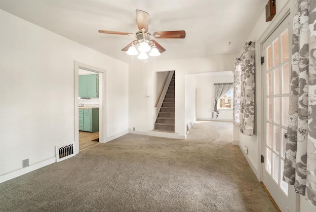 unfurnished room with visible vents, baseboards, stairway, carpet flooring, and a ceiling fan