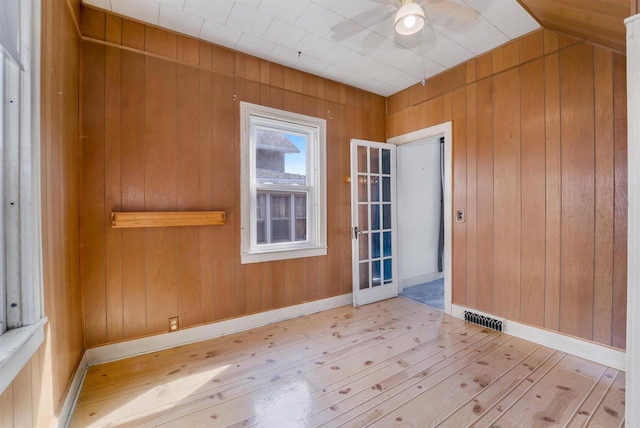 unfurnished room with hardwood / wood-style floors, visible vents, wood walls, and ceiling fan