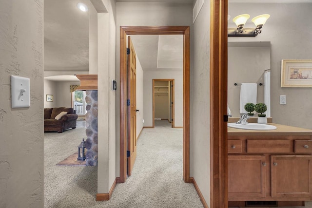 corridor with light carpet, a textured wall, baseboards, and a sink