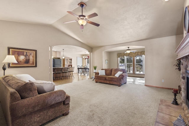 carpeted living area with baseboards, vaulted ceiling, a fireplace, arched walkways, and a ceiling fan