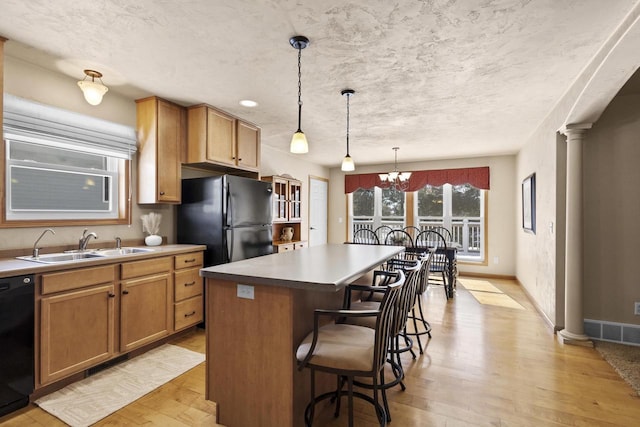 kitchen featuring light wood finished floors, decorative columns, a sink, black appliances, and a kitchen breakfast bar