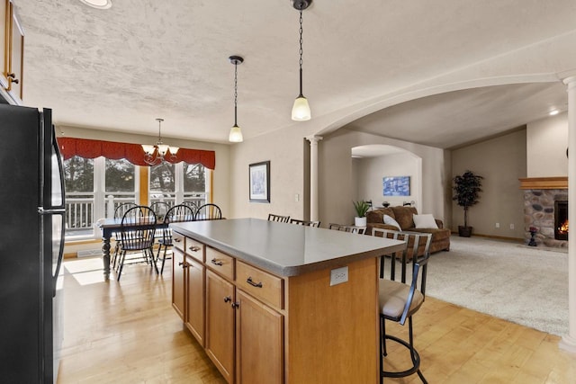 kitchen with a kitchen island, a breakfast bar, arched walkways, freestanding refrigerator, and open floor plan