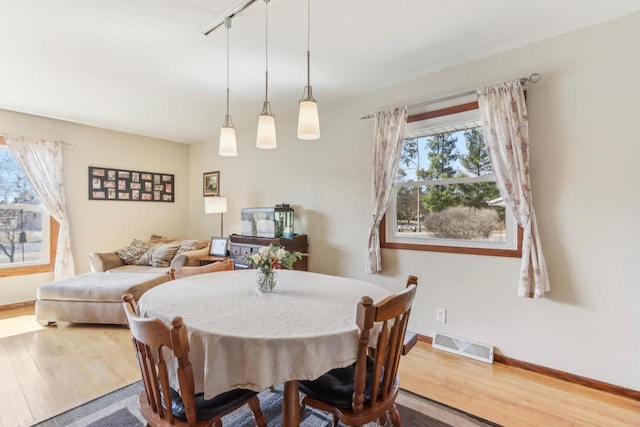 dining space featuring rail lighting, wood finished floors, visible vents, and baseboards