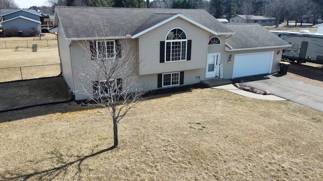 tri-level home with fence, a shingled roof, a front lawn, a garage, and aphalt driveway