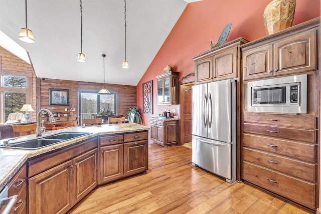 kitchen with light stone counters, light wood finished floors, a sink, stainless steel appliances, and decorative light fixtures