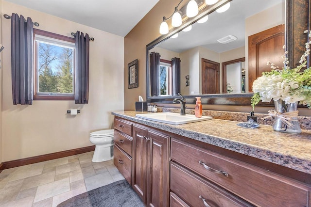 bathroom featuring vanity, visible vents, baseboards, stone finish floor, and toilet