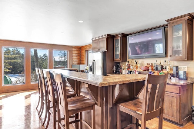 kitchen with a breakfast bar, rustic walls, stainless steel fridge, light countertops, and glass insert cabinets