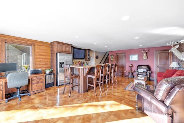 kitchen featuring finished concrete flooring, stainless steel fridge with ice dispenser, a breakfast bar, light countertops, and recessed lighting