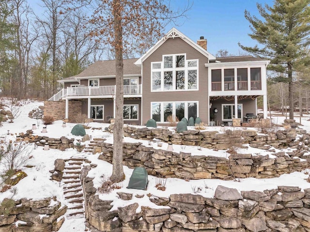 rear view of house with stairway, a deck, a chimney, and a sunroom