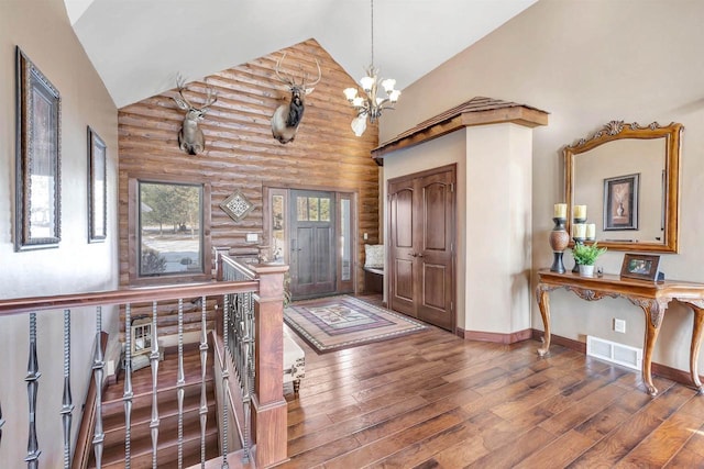 foyer entrance with visible vents, log walls, an inviting chandelier, high vaulted ceiling, and wood-type flooring