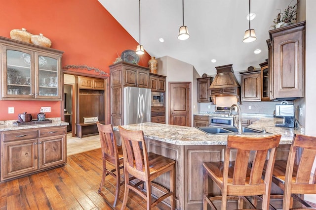 kitchen with custom exhaust hood, appliances with stainless steel finishes, glass insert cabinets, and hardwood / wood-style flooring